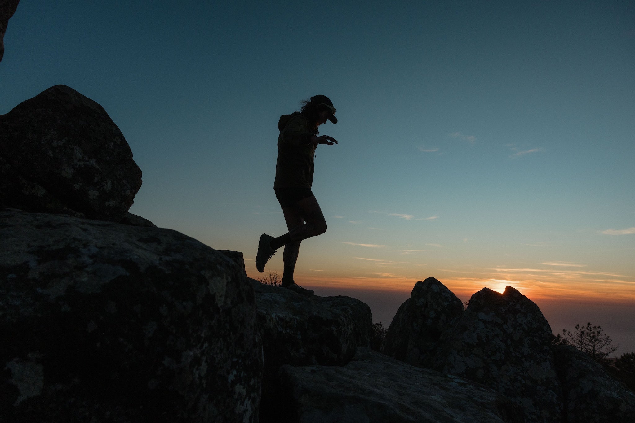 A woman silhouette jumping down some rocks at sunset