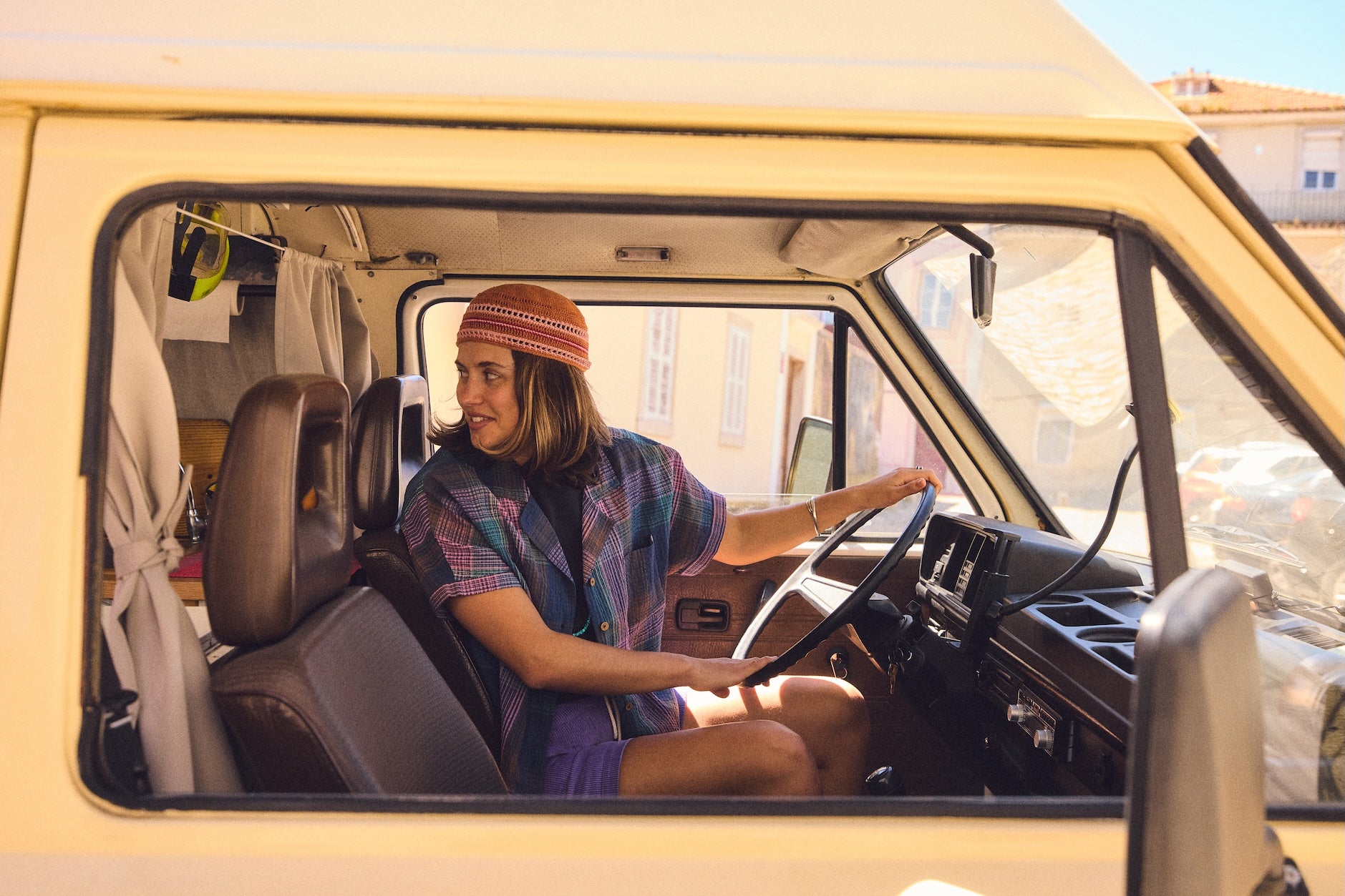 A woman sat in a van drivers seat looking back out the rear window and smiling