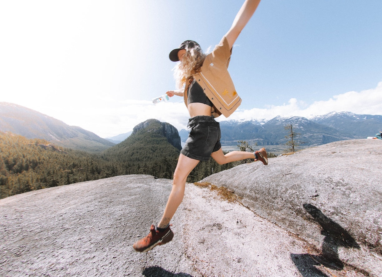 A woman wearing shorts jumping across a small ravine on a rock face
