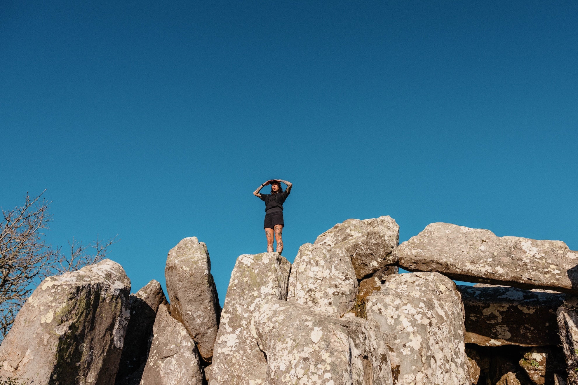 A woman standing on a rock face looking out over the landscape, blue sky behind her